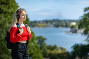 Henkilö seisoo kuulokkeet päässään ja kuntelee Celian äänikirjaa. Taustalla on aurinkoinen ja kesäinen merimaisema ja puita.