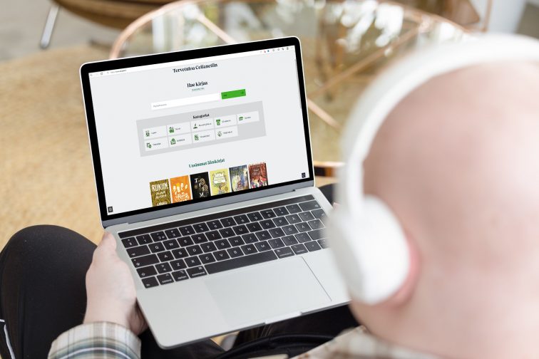 Takaapäin yläviistosta kuvattu henkilö, jolla on kannettava tietokone sylissään. Näytöllä on Celianetin etusivu. Henkilöllä on kuulokkeet korvillaan.